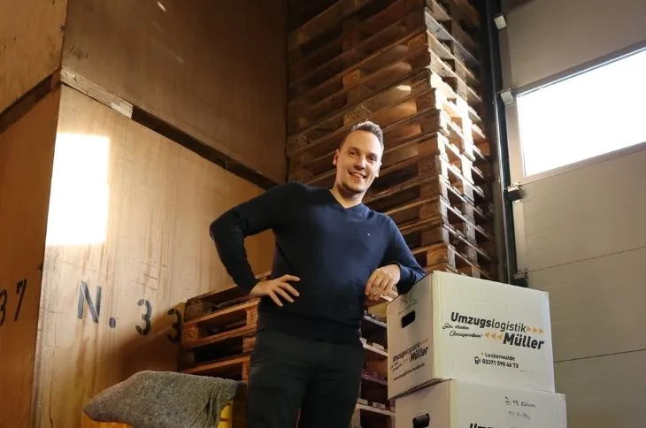 gluecklicher umzugshelfer steht vor umzugskartons im lager